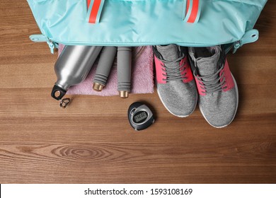 Open Sports Bag With Gym Stuff On Wooden Background, Flat Lay
