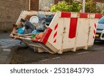 open steel industrial waste container filled with plastic bags and residual waste stands outside in a parking lot in a residential area