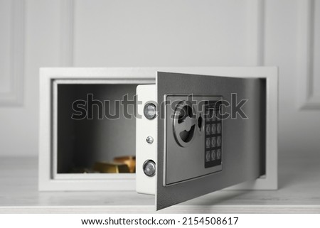 Open steel safe with gold bar and jewelry on wooden table