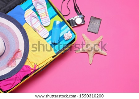 Open suitcase and beach objects on pink background, flat lay