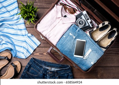Open suitcase with casual female clothes on wooden table