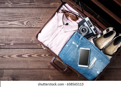 Open Suitcase With Casual Female Clothes On Wooden Table