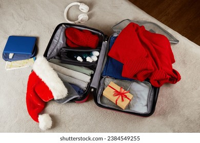 An open suitcase with clothes, documents, a gift, a Santa Claus hat. Packing things, preparing for a trip for the Christmas holidays. The concept of travel.