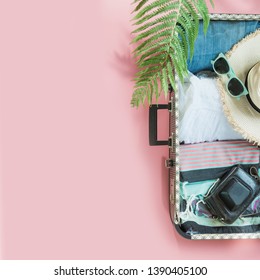 Open Suitcase With Female Clothes, Leaf Of Fern, Tropical Detox Water On Pastel Pink. Top View With Copy Space. Summer Travel Concept.