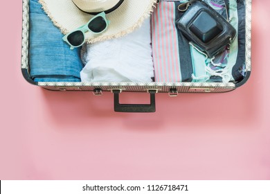 Open Suitcase With Female Clothes For Trip On Pastel Pink Background. Top View With Copy Space. Summer Concept Travel.