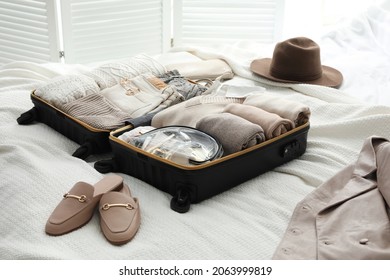 Open Suitcase With Folded Clothes, Shoes And Accessories On Bed