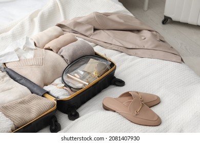 Open Suitcase With Folded Clothes, Shoes And Accessories On Bed In Room