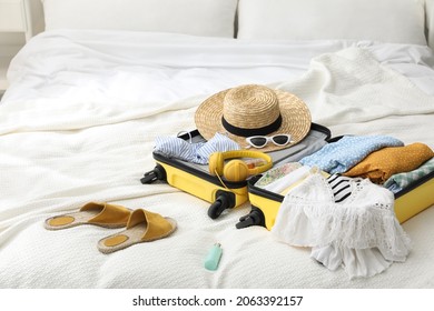 Open Suitcase Full Of Clothes, Shoes And Summer Accessories On Bed