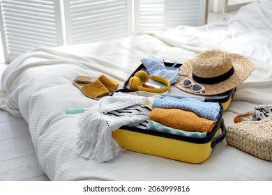 Open Suitcase Full Of Clothes, Shoes And Summer Accessories On Bed