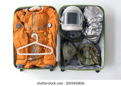 Open Suitcase Packed For Space Travelling With Astronaut Orange Space Suit, Space Helmet And Spacesuit Accessories On White Background. Funny Space Tourism Concept.