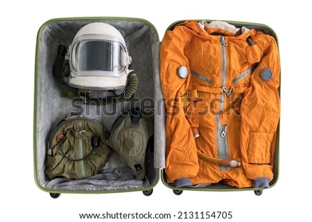Open suitcase packed for space travelling with astronaut orange space suit, space helmet and spacesuit accessories isolated on white background. Top view. Fun space tourism concept.