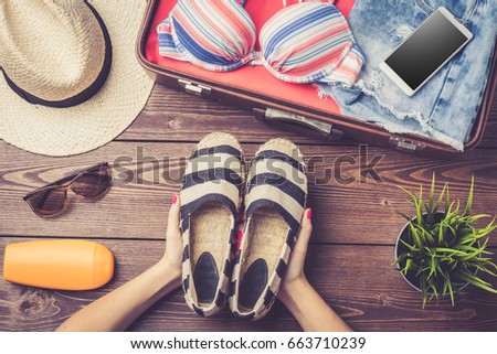 Open suitcase with summer or beach clothes and accessories on wooden table