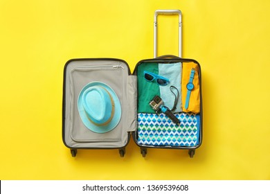 Open Suitcase With Summer Clothes And Accessories On Color Background, Top View