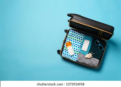 Open suitcase with traveler's belongings on color background, top view. Space for text