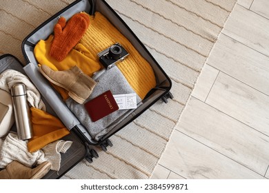 Open suitcase with travelling accessories and winter clothes on carpet, top view