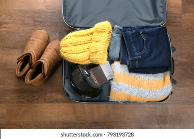 Open suitcase with warm clothes, ski goggles and documents on wooden floor. Winter vacation concept - Powered by Shutterstock