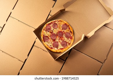 Open Takeaway Box With Freshly Made Italian Salami Pizza Inside On A Background Of Generic Brown Cardboard Pizza Boxes Viewed Top Down In A Flat Lay Still Life