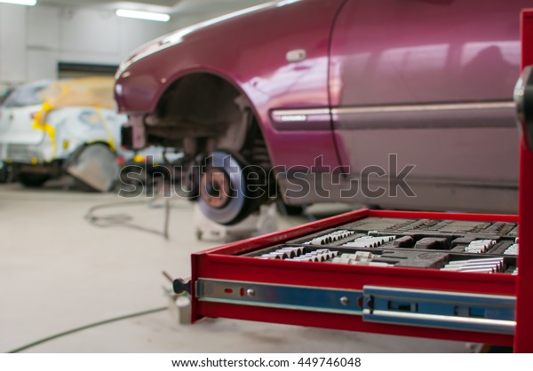Open tool box in a garage with a car repair in\
progress in the background