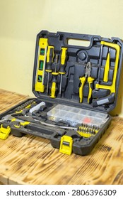 Open tool kit featuring various hand tools such as screwdrivers and pliers, placed on a wooden surface with a plain wall in the background