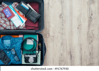 Open traveler's bag with clothing, accessories, credit card, tickets and passport, travel and vacations concept, flat lay