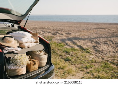 Open Trunk Of Car With Picnic Items: Straw Hat, Basket With Food And Flowers With Summer Beach On The Background. Place For Text.