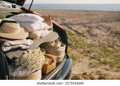 Open Trunk Of Car With Picnic Items: Straw Hat, Basket With Food And Flowers With Summer Beach On The Background. Place For Text.