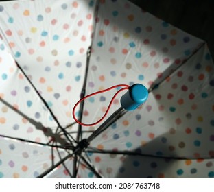 An Open Umbrella Photographed From The Inside. We See A Blue Handle. The Umbrella Is White And Has Colored Polka Dots On It.