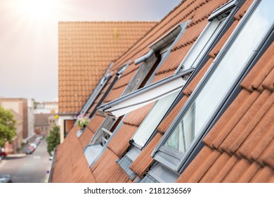 Open ventilation waterproof rooftop window exterior against sunny sky light. Velux style roof with red brick tiles. European city street attic mansard modern roofwindow service, install maintenance
