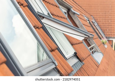 Open ventilation waterproof rooftop window exterior against sunny sky light. Velux style roof with red brick tiles. European city street attic mansard modern roofwindow service, install maintenance