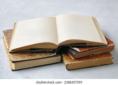 An Open Vintage Book With Blank Pages Or A Dust Jacket Notebook On A Stack Of Old Shabby Books On A Gray Concrete Table. Mockup Layout