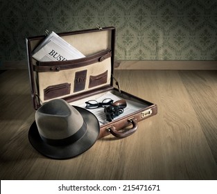 Open vintage leather briefcase with detective hat, revolver gun and newspaper.