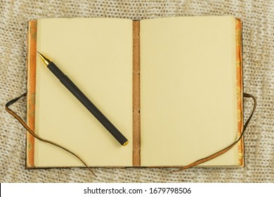 Open vintage notebook and pen on beige knit fabric background top view flat lay