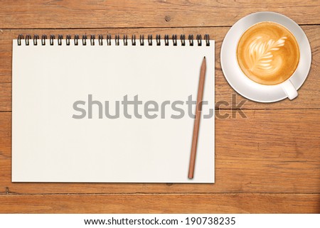 An open vintage sketchbook or notebook with pencil and a cup of coffee on modern wooden table. latte art on top.