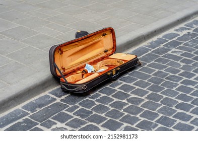 Open violin case lies on old cobblestone in city. Street musician collects money