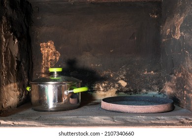 Open volume of an old wood-burning stove for cooking. The walls of the oven are covered with soot and soot. Inside is a modern metal saucepan with green handles. Background. 