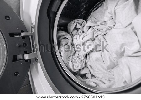 Open washer with bedding. White sheets inside drum. Household laundry process scene. Clean fabric care view. Modern appliance interior detail. Domestic washing routine concept.