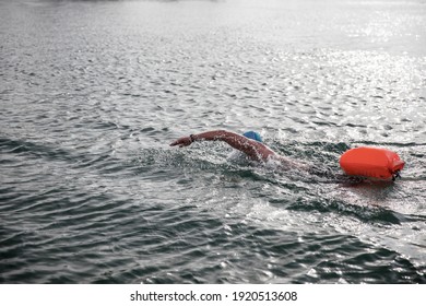 Open water swimmer swimming in the lake with red safety bag and  with a blue swimming cap