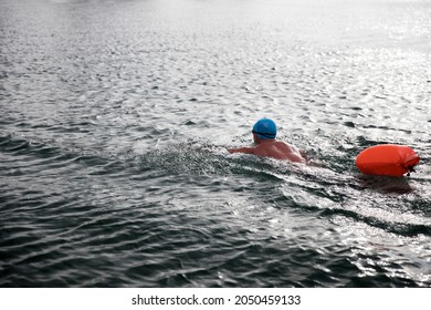 Open water swimmer swimming in the water with red safety bag and  with a blue swimming cap in misty weather