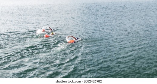 Open Water Swimmers Swimming In The Water With Red Safety Bag And  With A Swimming Cap In The Lake, Ocean