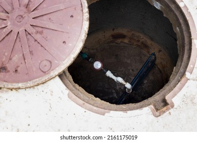 An Open Water Well With A Water Metering Unit Carried Into The House. Taking Water Meter Readings.