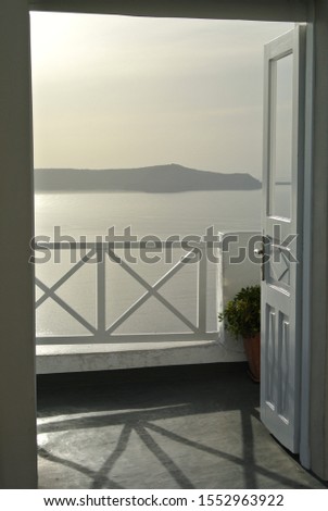 An open white door leading to a terrace with a beautiful view on the pearl sea waters at the sunset on the Santorini island in Greece
