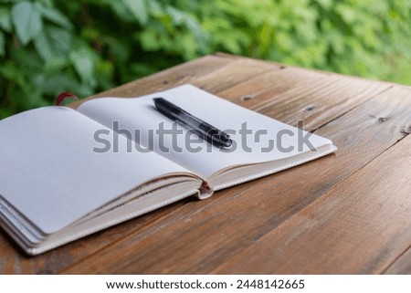 Open white empty paper notepad on wooden table outdoors. Concept of author writing in relaxed cozy atmosphere. Spiritual health digital detox slowing down