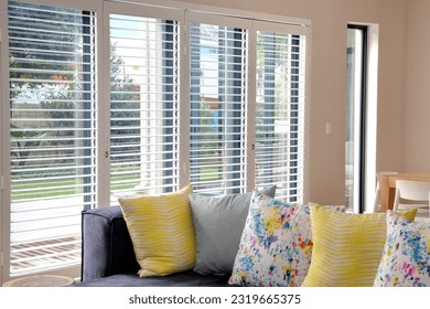 
Open white shutters in living room, with blue couch and yellow scatter cushions
