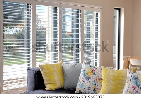 
Open white shutters in living room, with blue couch and yellow scatter cushions