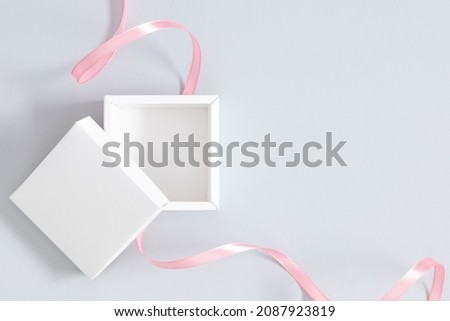 Open white square box mockup with pink ribbon on gray background. Flat lay, top view, copy space