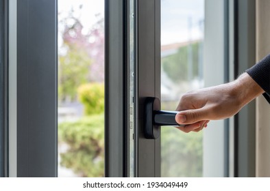 Open the window.  Hand and aluminum frame closeup view. Man holding the metal or PVC door handle. Energy efficient, security profile, blur garden outdoor background