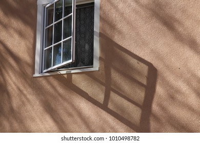 Open window with lace casting shadows on an adobe wall
