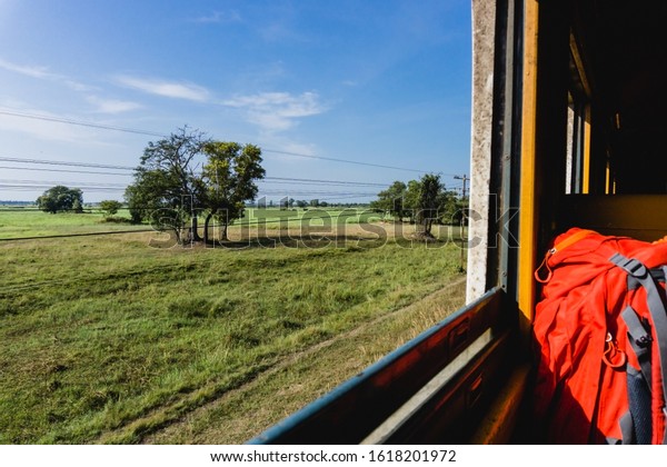 Open window train travel. Sunny summer in Thailand.\
Idyllic meadow landscape. Travelling with big backpack. Through the\
window view.