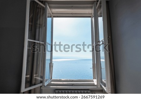 Open window with a view of calm blue sea and clear sky, symbolizing relaxation, freedom, travel, and peaceful summer vacation by the ocean.