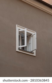 An open window with a white frame stands out on a solid brown stucco building facade. This house casement provides fresh air and ventilation. Clean residential property exterior architecture.